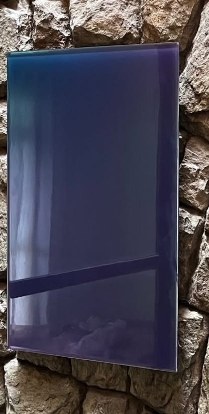 Espelho retangular em azul-violeta numa parede de pedra, refletindo uma janela.